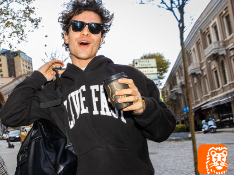 Jongen met zonnebril en koffiebeker loopt door de straat