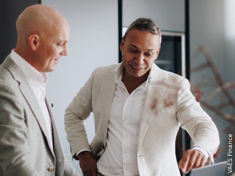 Twee mannen in gesprek beide hebben lichte kleding aan met kijken naar een scherm